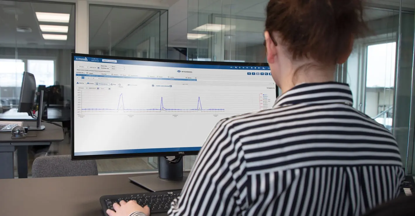 Person monitoring real-time temperature data on a computer screen using a cold chain tracking dashboard in an office setting.